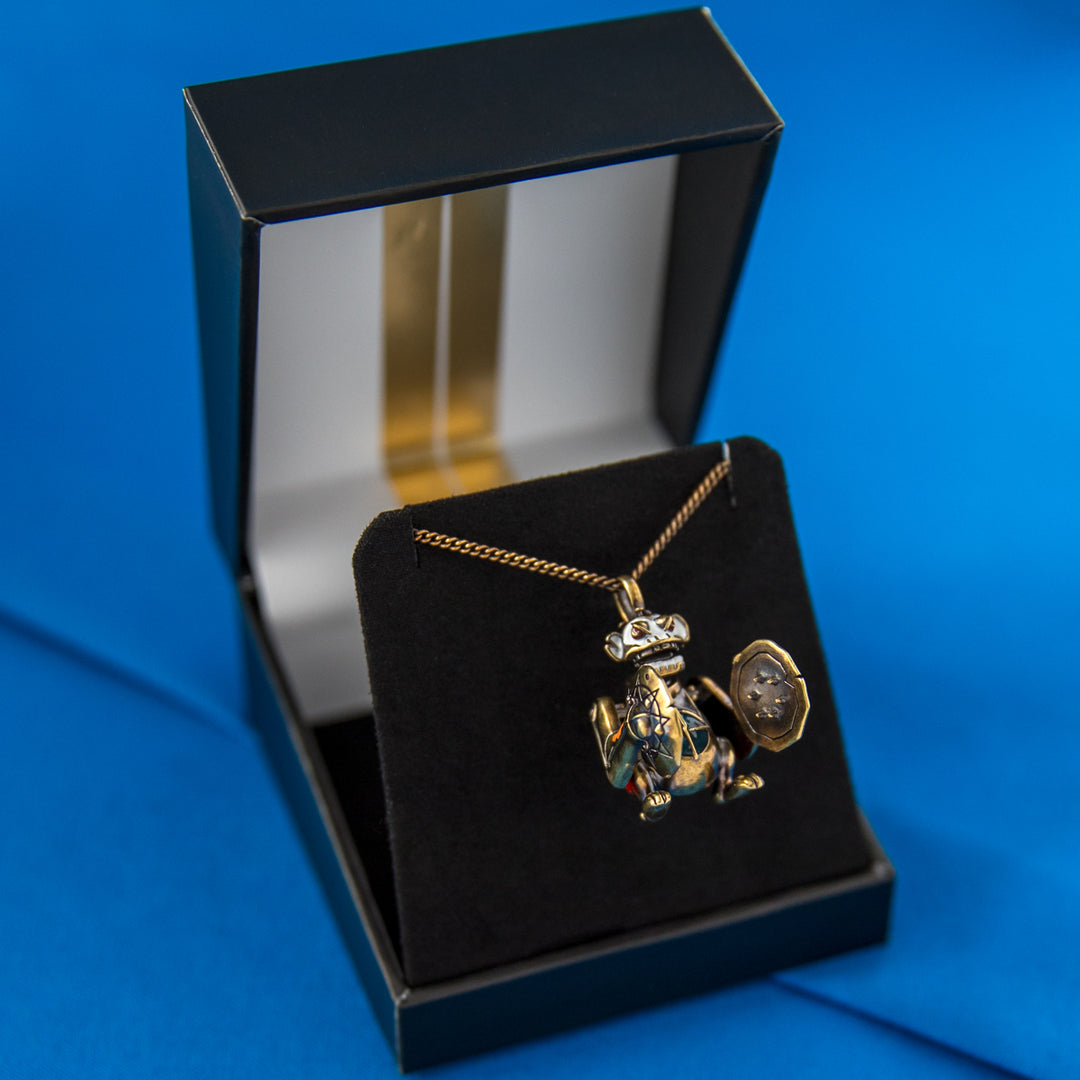 Arcane × RockLove Jinx Monkey necklace in open ARCANE Collector’s Box showing bronze pendant, enamel details, and metallic gold art inside the lid.