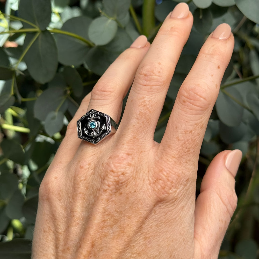 Hand wearing a decorative ring with a blue crystal against a leafy background