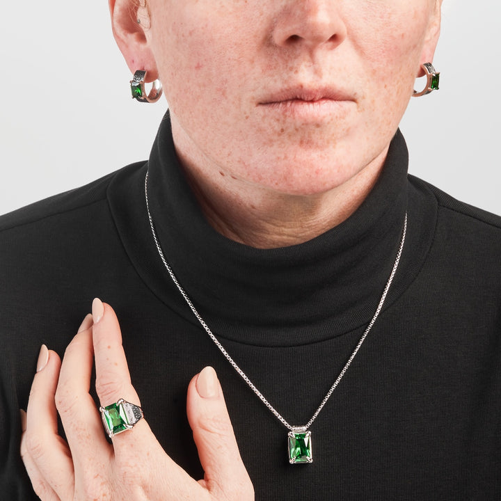 Person wearing a black turtleneck with green gemstone jewelry on a plain background