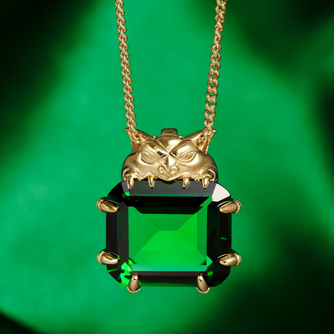 Magic: The Gathering X RockLove Mox Emerald Necklace —  Emerald set in 14K gold plated sterling silver, [context: a gold pendant necklace featuring a creature above a large, faceted green rectangular gemstone, shown against a vibrant green background.]
