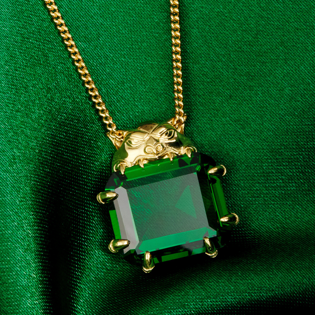 Magic: The Gathering X RockLove Mox Emerald Necklace —  Emerald set in 14K gold plated sterling silver, [context: a gold pendant necklace featuring a large, faceted green rectangular gemstone with gold prongs, resting on a draped green satin fabric background.]