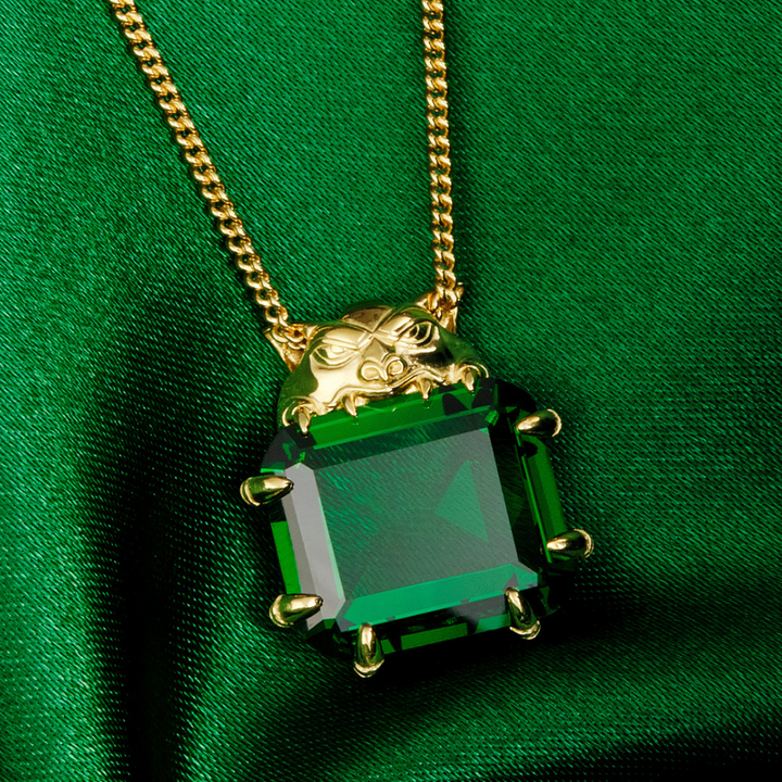 Magic: The Gathering X RockLove Mox Emerald Necklace —  Emerald set in 14K gold plated sterling silver, [context: a gold pendant necklace featuring a large, faceted green rectangular gemstone with gold prongs, resting on a draped green satin fabric background.]