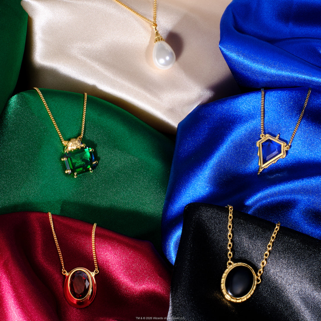Magic: The Gathering X RockLove Mox Pearl, Sapphire, Jet, Ruby, and Emerald Necklaces — set in 14K gold
plated sterling silver, [context: Five gold pendant necklaces displayed on draped satin fabric in beige, green, blue, red, and black. The necklaces feature distinct pendants: a white pearl, a rectangular green gemstone, an oval red gemstone, and a geometric blue gemstone.]
