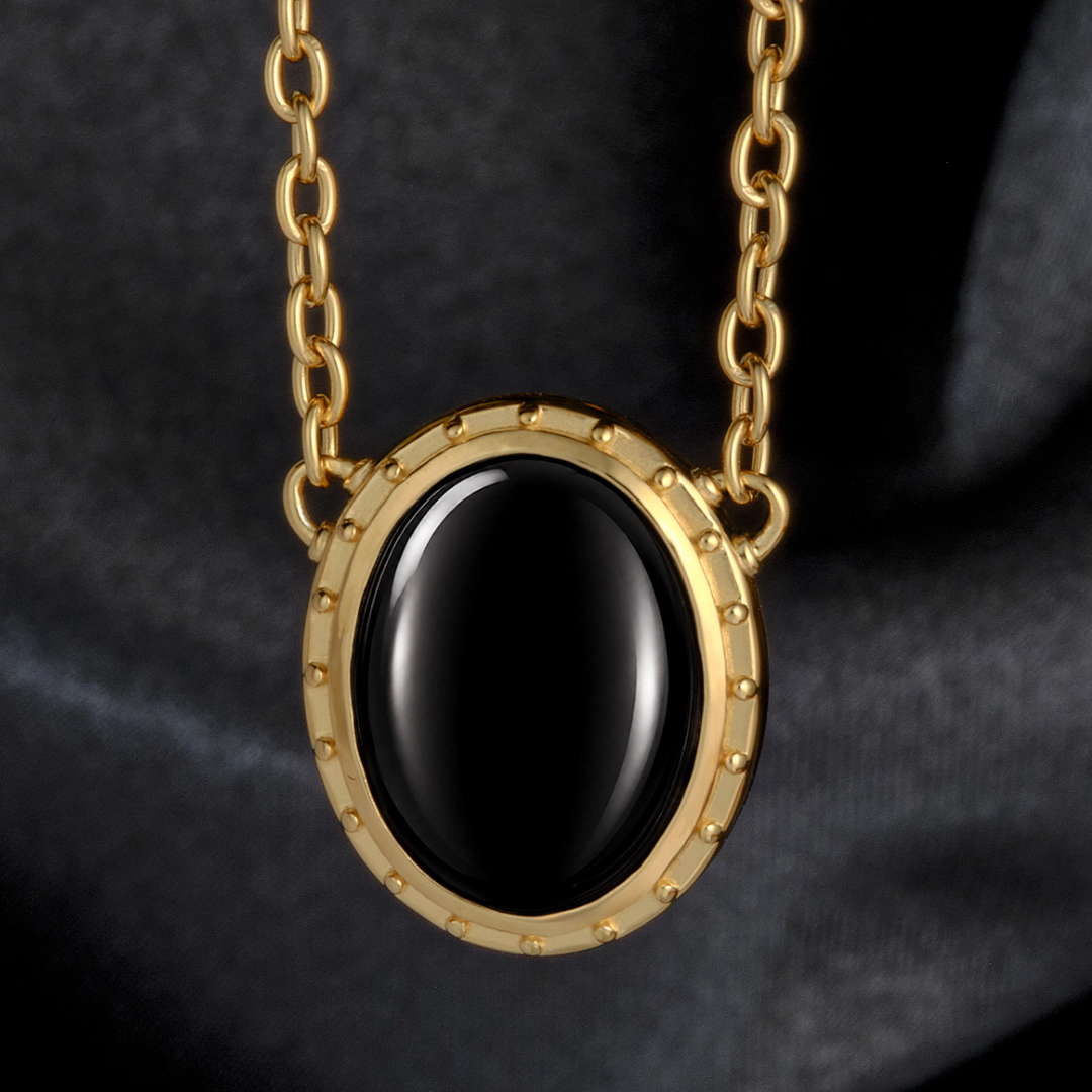 Magic: The Gathering X RockLove Mox Jet Necklace — Onyx set in 14K gold
plated sterling silver, [context: a gold chain necklace with an oval black stone pendant, set in a gold bezel with small raised studs, shown against a dark gray fabric background.]