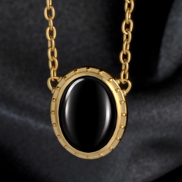 Magic: The Gathering X RockLove Mox Jet Necklace — Onyx set in 14K gold
plated sterling silver, [context: a gold chain necklace with an oval black stone pendant, set in a gold bezel with small raised studs, shown against a dark gray fabric background.]