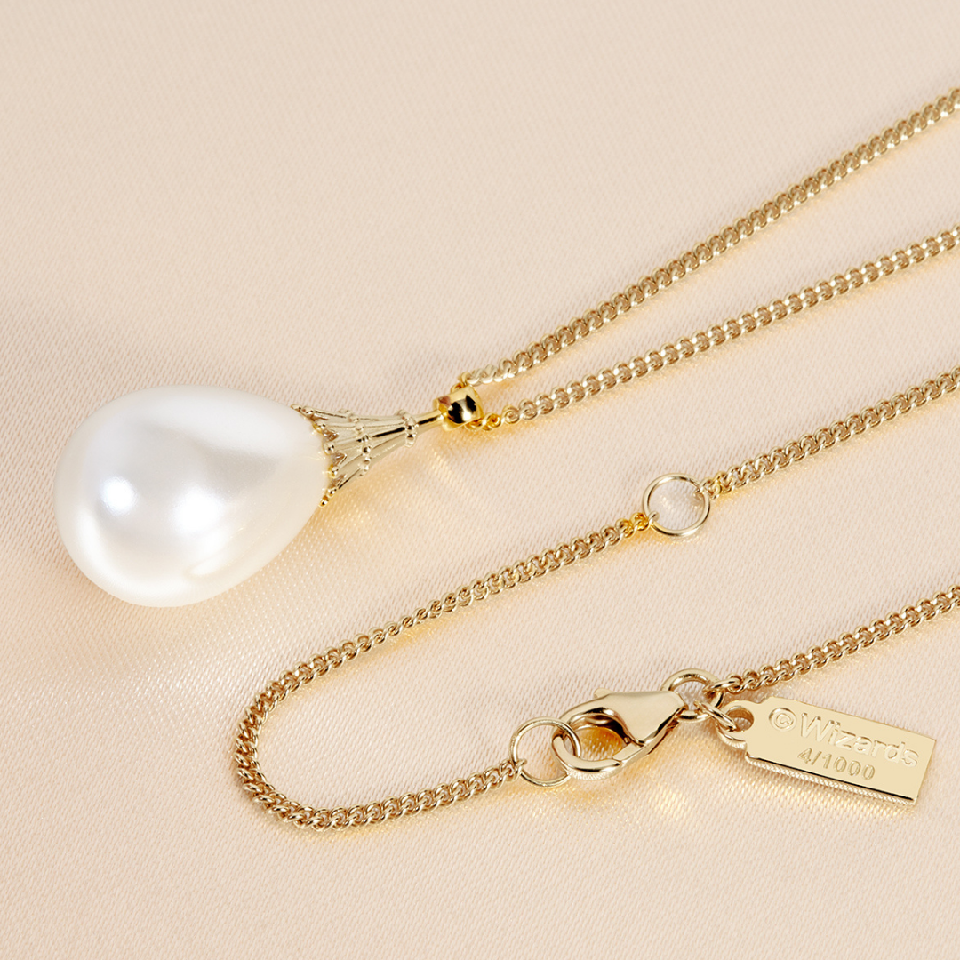 Magic: The Gathering X RockLove Mox Pearl Necklace — Pearl set in 14K gold
plated sterling silver, [context: gold chain necklace with a teardrop-shaped white pearl pendant and a gold clasp, shown on a light beige fabric background. A small numbered brand tag is attached to the clasp.]