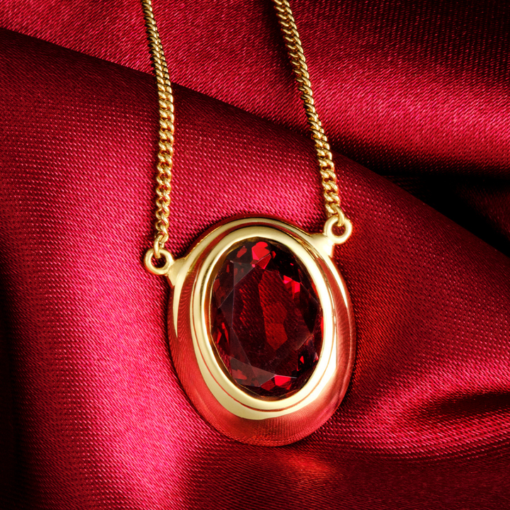 Magic: The Gathering X RockLove Mox Ruby Necklace —  Ruby set in 14K gold
plated sterling silver, [context: gold oval pendant necklace with a faceted red gemstone, displayed on draped red satin fabric.]
