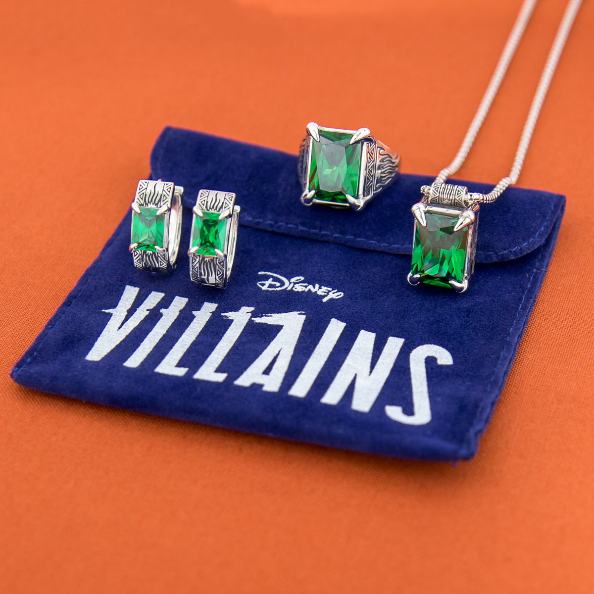 Jewelry set with green gemstones on a 'Disney Villains' branded pouch.