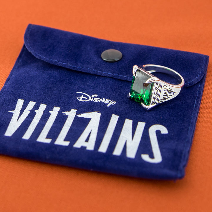 Silver ring with a green gemstone on a blue 'Disney Villains' pouch against an orange background